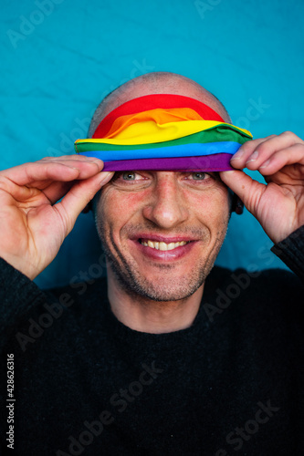 Cheerful smiling Caucasian gay man with rainbow protective face mask on forehead