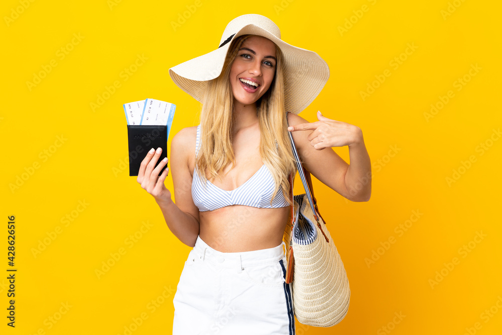 Young Uruguayan blonde woman in swimsuit holding a passport over isolated yellow background and pointing it Young Uruguayan blonde woman in swimsuit holding a passport over isolated yellow background and pointing it