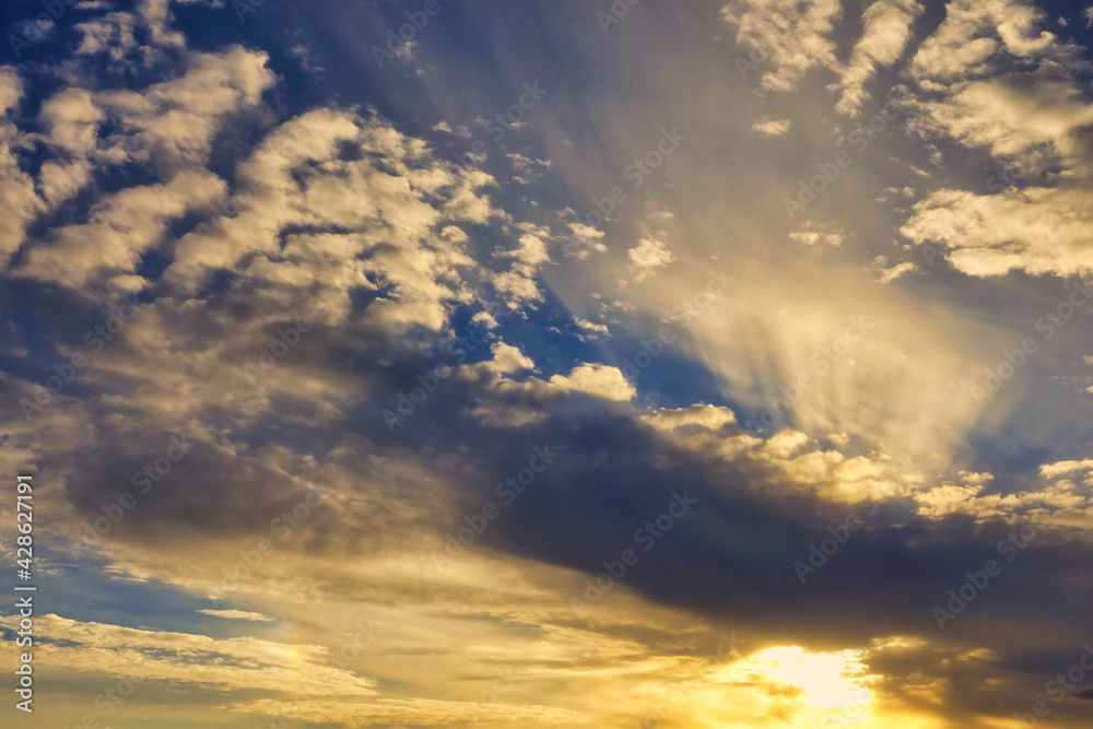 Fototapeta premium Blue sky with clouds and sunbeams at sunset