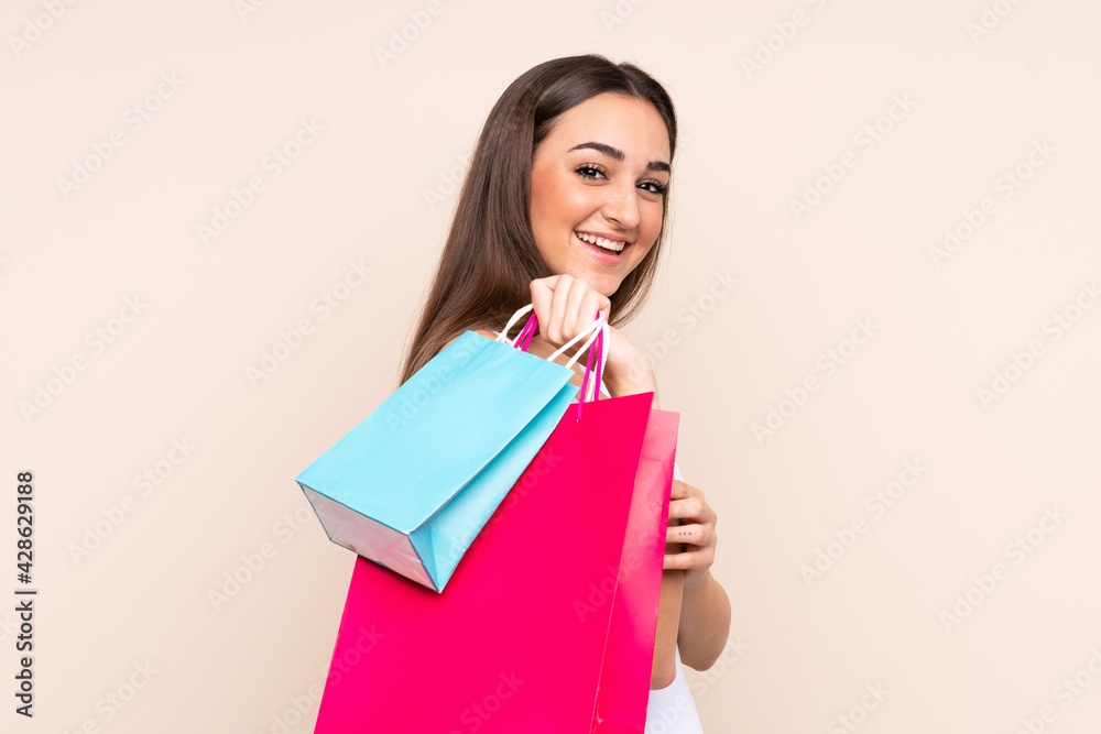 Young caucasian woman isolated on beige background holding shopping bags and looking back Young caucasian woman isolated on beige background holding shopping bags and looking back
