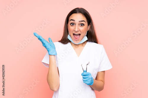 Woman dentist holding tools isolated on pink background with surprise facial expression