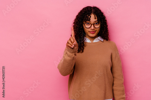Young mixed race woman isolated on pink background showing number one with finger. © Asier