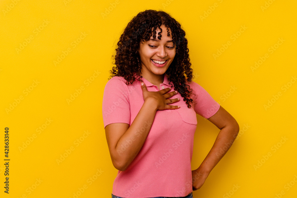 Young mixed race woman isolated on yellow background laughing keeping hands on heart, concept of happiness. Young mixed race woman isolated on yellow background laughing keeping hands on heart, concept of happiness.