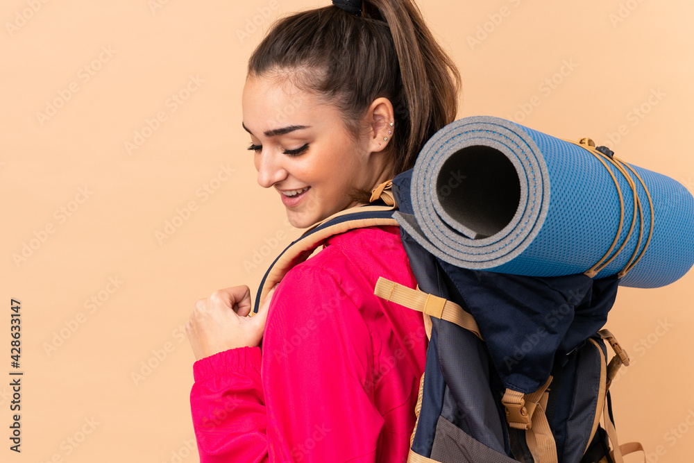 Fototapeta premium Young mountaineer girl with a big backpacker isolated on beige background