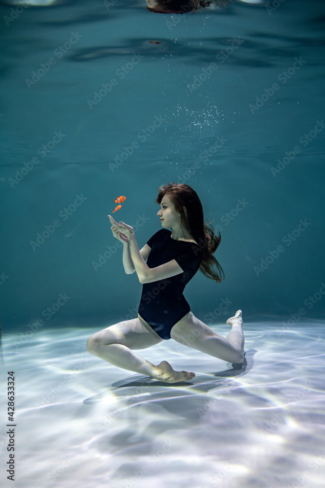 beautiful girl in a black swimsuit plays in orange fish underwater on a blue background 