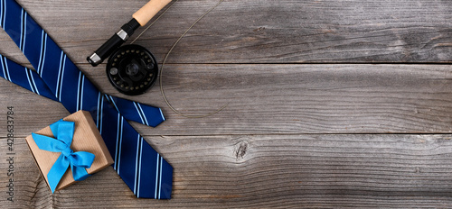 Fathers day concept with blue dress tie, fly fishing reel and a giftbox on rustic wooden background