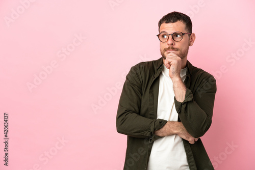 Young Brazilian man isolated on pink background having doubts and thinking