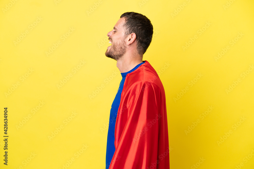 Super Hero Brazilian man isolated on yellow background laughing in lateral position Super Hero Brazilian man isolated on yellow background laughing in lateral position