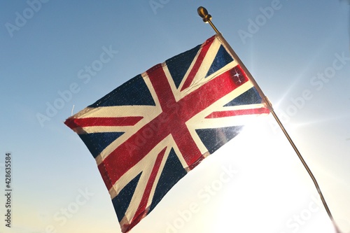 Distressed old UK Great Britain flag against the sunny sky. Symbol of United Kingdom. Weathered British Union Jack. Perfect stock photo for illustrating negative news about royal family