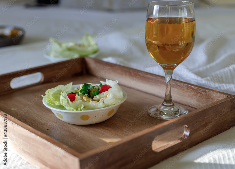 Lettuce egg wrap on a brown tray in room with a glass of drink on bed