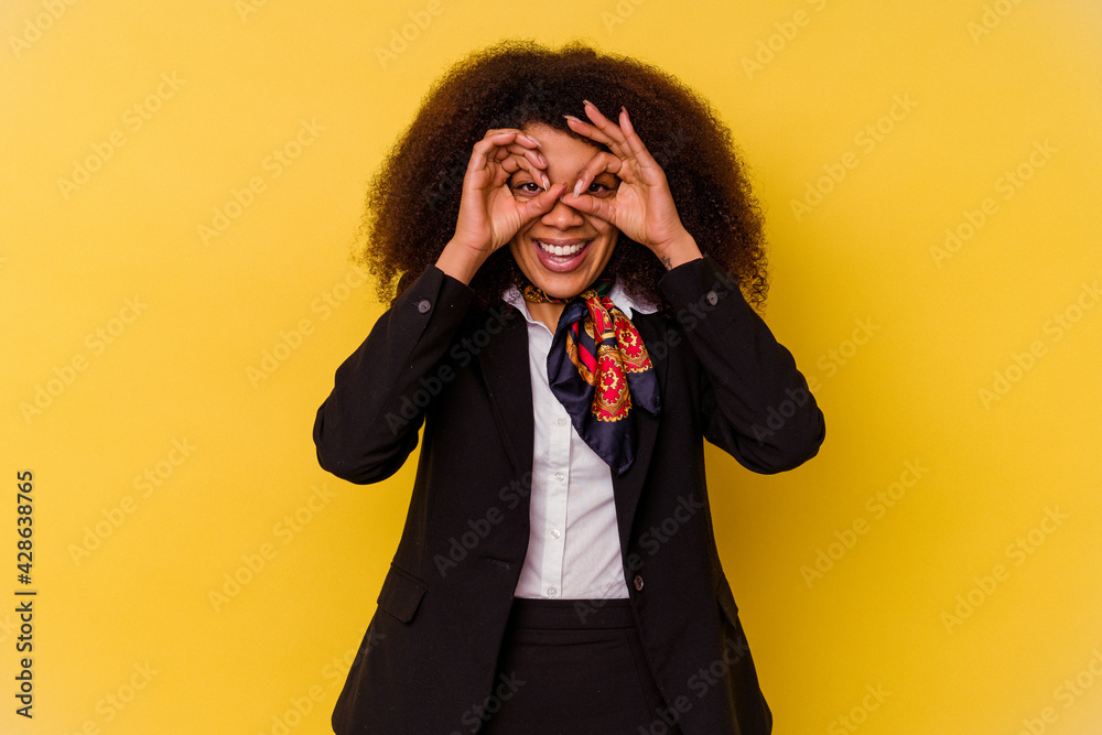 Young African American air hostess isolated on yellow background showing okay sign over eyes Young African American air hostess isolated on yellow background showing okay sign over eyes