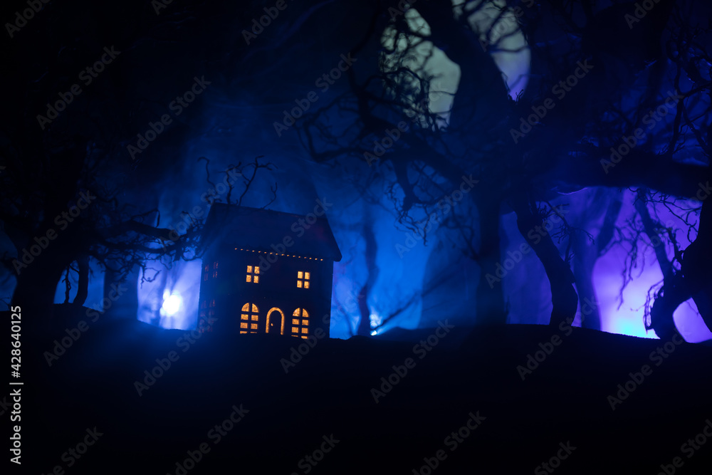 Old house with a Ghost in the forest at night or Abandoned Haunted Horror House in fog. Old mystic building in dead tree forest. Trees at night with moon. Surreal lights. Horror Halloween concept