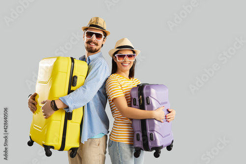 Happy smiling couple or friends tourist in summer hat and sunglasses holding luggage bag ready for trip studio shot on grey background with copy space. Vacation time, travel and tourism photo