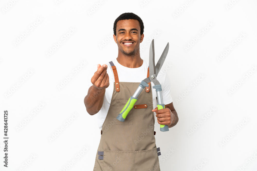 African American gardener man holding pruning shears over isolated white background making money gesture African American gardener man holding pruning shears over isolated white background making money gesture
