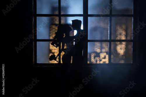 A realistic dollhouse living room with furniture and window at night. Romantic couple sitting on window. Artwork table decoration with handmade realistic dollhouse. Selective focus.