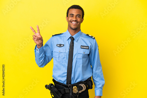 African American police man over isolated yellow background smiling and showing victory sign