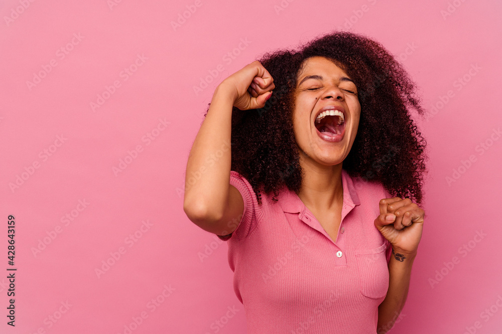 Young african american woman isolated on pink background raising fist after a victory, winner concept. Young african american woman isolated on pink background raising fist after a victory, winner concept.