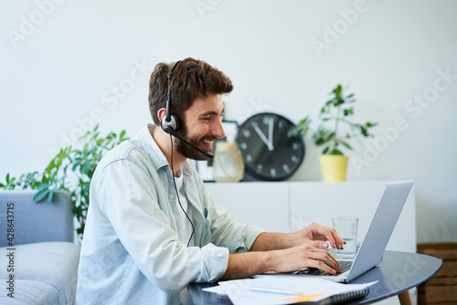 Home office concept. Young man with headset working remotely using laptop photo