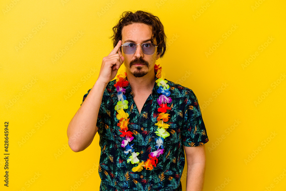 Obraz premium Young caucasian man wearing a hawaiian necklace isolated on yellow background pointing temple with finger, thinking, focused on a task.