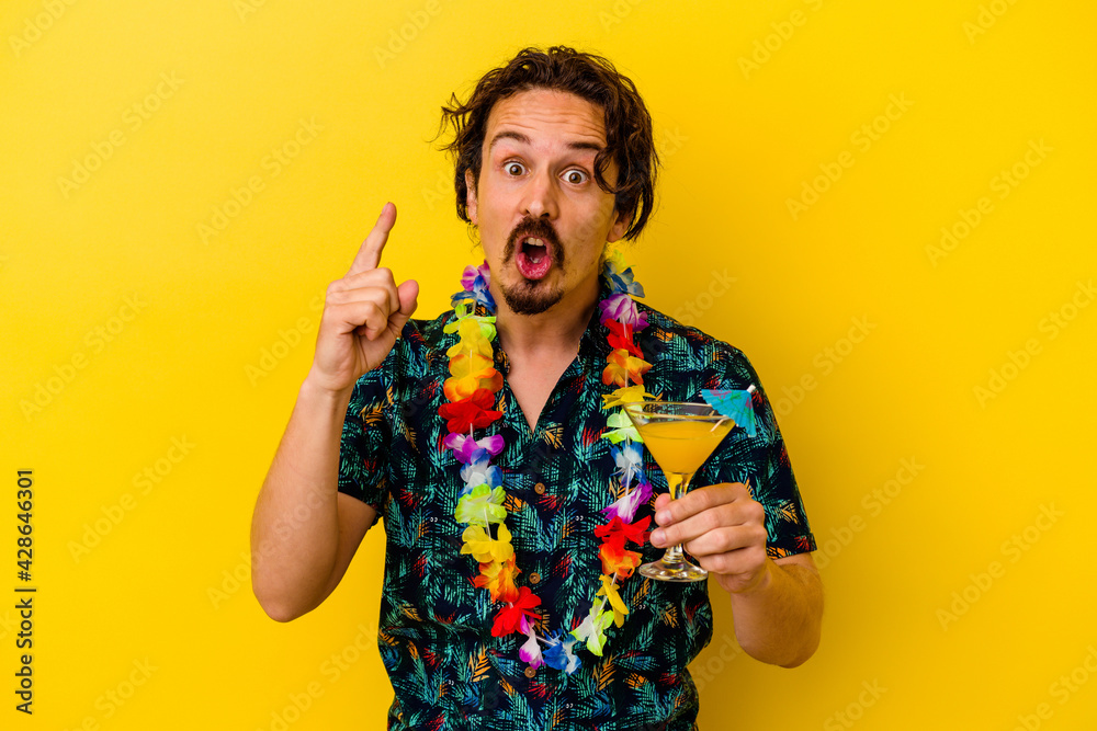 Young caucasian man wearing a hawaiian necklace holding a cocktail isolated on yellow background having an idea, inspiration concept. Young caucasian man wearing a hawaiian necklace holding a cocktail isolated on yellow background having an idea, inspiration concept.