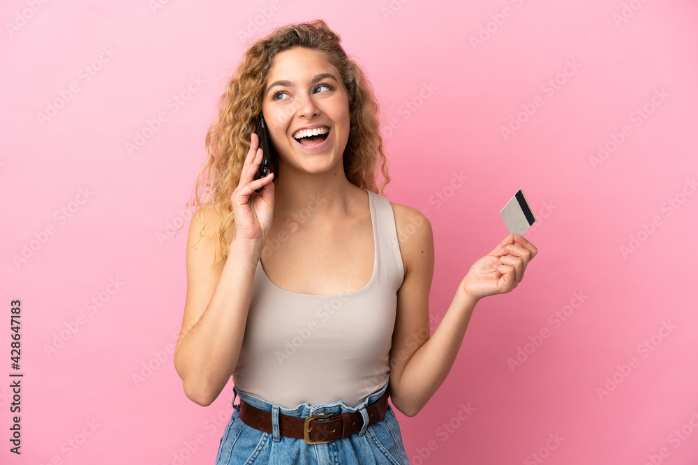 Young blonde woman isolated on pink background keeping a conversation with the mobile phone and holding a credit card Young blonde woman isolated on pink background keeping a conversation with the mobile phone and holding a credit card