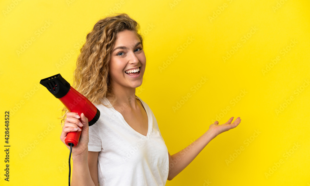 Young blonde woman holding a hairdryer isolated on yellow background extending hands to the side for inviting to come
