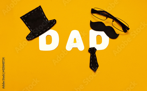 Happy Father's Day concept. Black hat, tie, mustache, word English DAD, handmade. Composition on a yellow background.