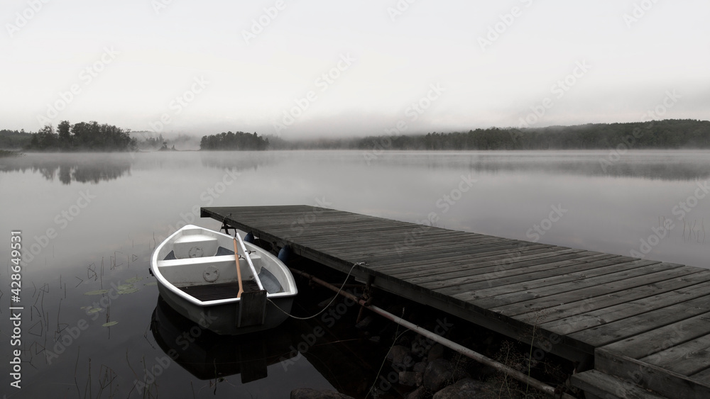 A lone rowboat on a misty lake next to a pier.