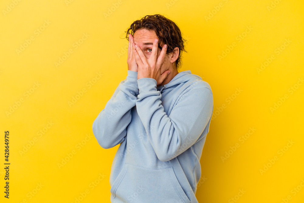 Young caucasian man isolated on yellow background blink through fingers frightened and nervous. Young caucasian man isolated on yellow background blink through fingers frightened and nervous.