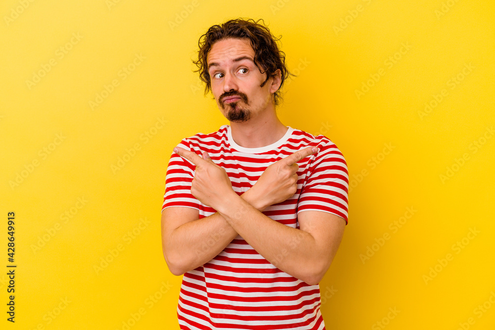 Young caucasian man isolated on yellow background points sideways, is trying to choose between two options. Young caucasian man isolated on yellow background points sideways, is trying to choose between two options.