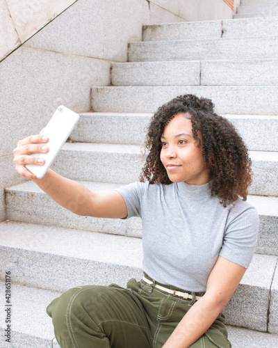A woman with curly hair taking a selfie smiling while sitting on a staircase.