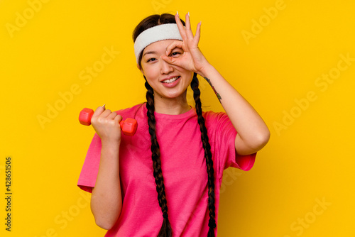 Young sport chinese woman isolated on yellow background excited keeping ok gesture on eye.