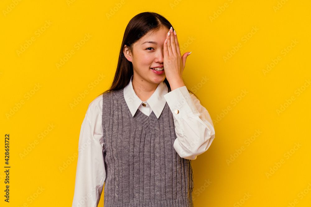 Young chinese woman isolated on yellow background having fun covering half of face with palm. Young chinese woman isolated on yellow background having fun covering half of face with palm.