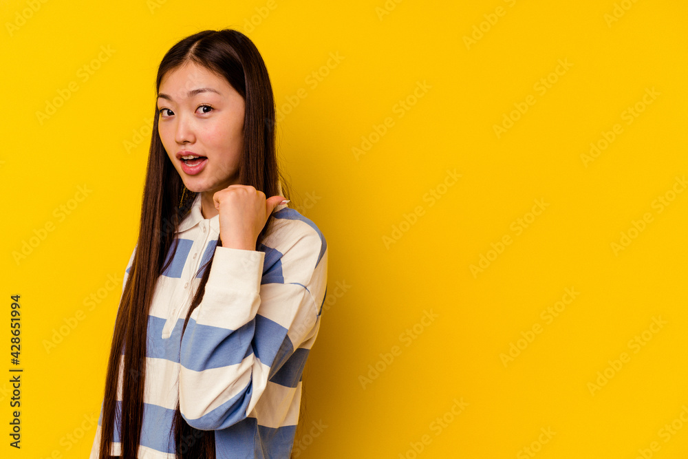 Young chinese woman isolated on yellow background points with thumb finger away, laughing and carefree. Young chinese woman isolated on yellow background points with thumb finger away, laughing and carefree.