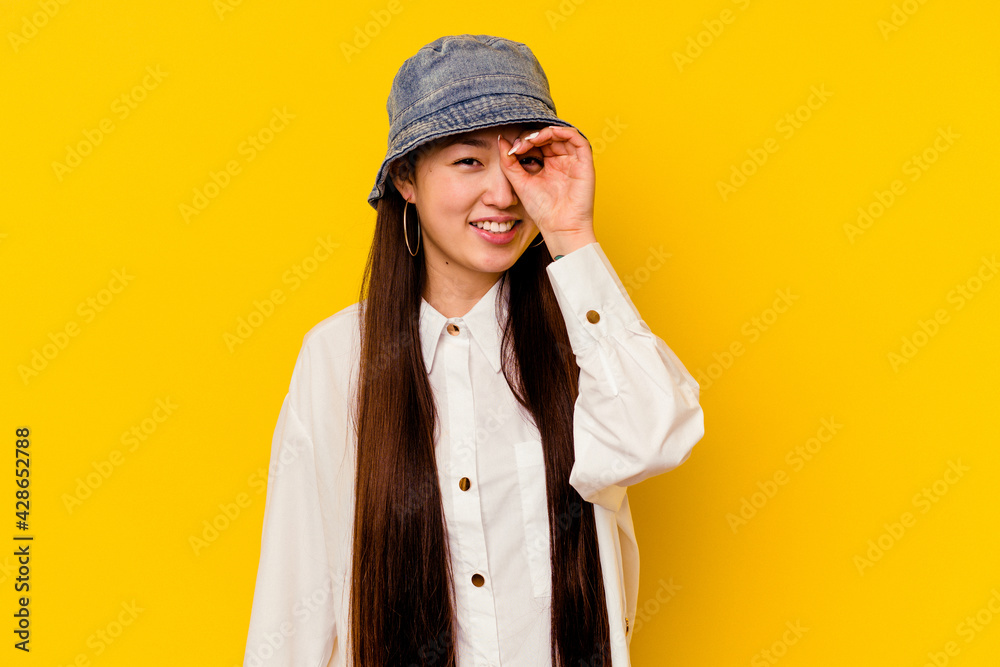 Young chinese woman isolated on yellow background showing okay sign over eyes Young chinese woman isolated on yellow background showing okay sign over eyes