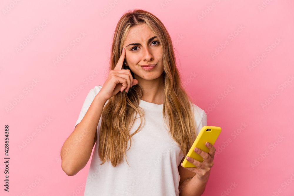 Young blonde caucasian woman holding a yellow mobile phone isolated pointing temple with finger, thinking, focused on a task. Young blonde caucasian woman holding a yellow mobile phone isolated pointing temple with finger, thinking, focused on a task.