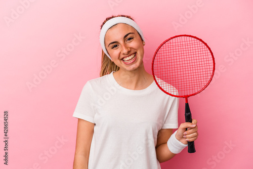 Young cute blonde caucasian woman holding a badminton racket isolated on pink background happy, smiling and cheerful.