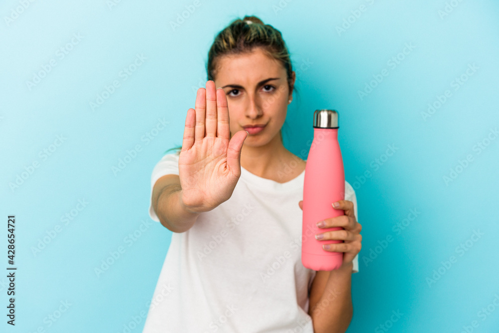 Young blonde caucasian woman holding a thermo isolated on blue background standing with outstretched hand showing stop sign, preventing you.