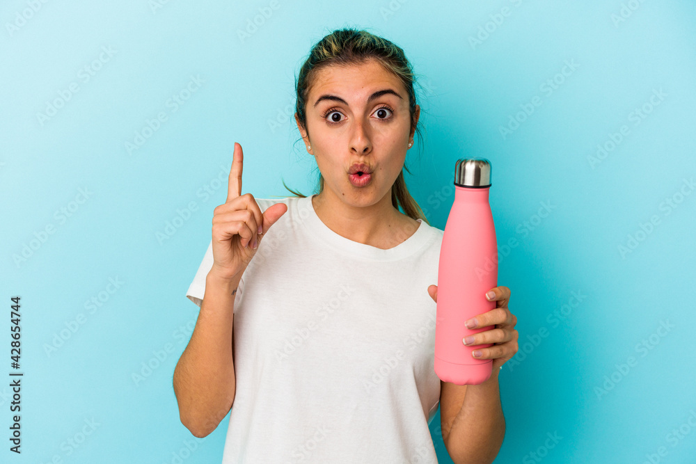 Young blonde caucasian woman holding a thermo isolated on blue background having some great idea, concept of creativity. Young blonde caucasian woman holding a thermo isolated on blue background having some great idea, concept of creativity.