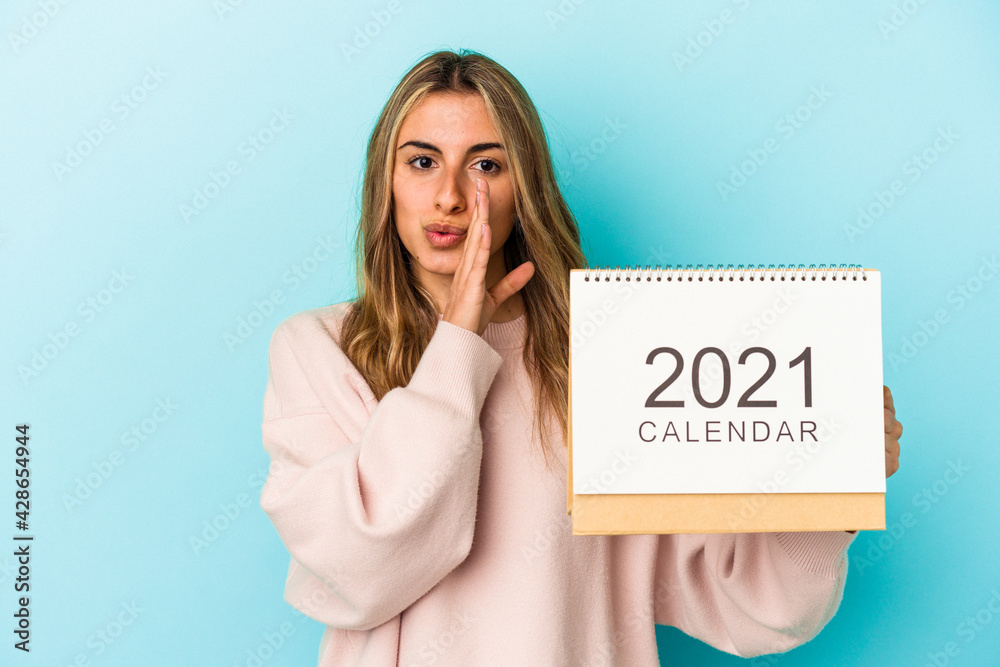 Young blonde caucasian woman holing a calendar isolated is saying a secret hot braking news and looking aside