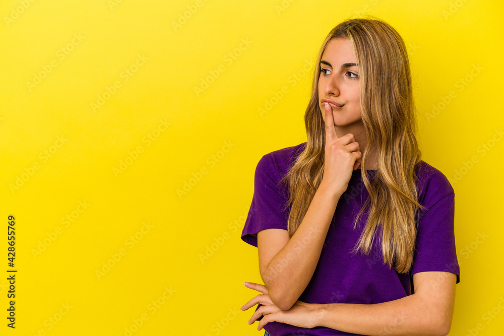 Young blonde caucasian woman isolated on yellow background looking sideways with doubtful and skeptical expression. Young blonde caucasian woman isolated on yellow background looking sideways with doubtful and skeptical expression.
