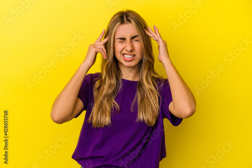 Young blonde caucasian woman isolated on yellow background touching temples and having headache.