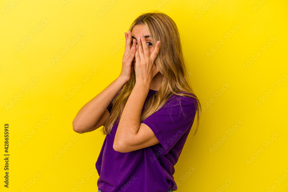 Young blonde caucasian woman isolated on yellow background blink through fingers frightened and nervous. Young blonde caucasian woman isolated on yellow background blink through fingers frightened and nervous.
