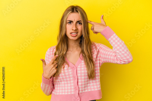 Young blonde caucasian woman isolated on yellow background showing a disappointment gesture with forefinger.