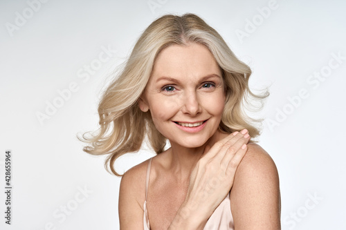 Happy smiling adult 50s aged woman looking at camera with hand on her shoulder portrait isolated on white background. Hair and skin anti age care products advertising concept.