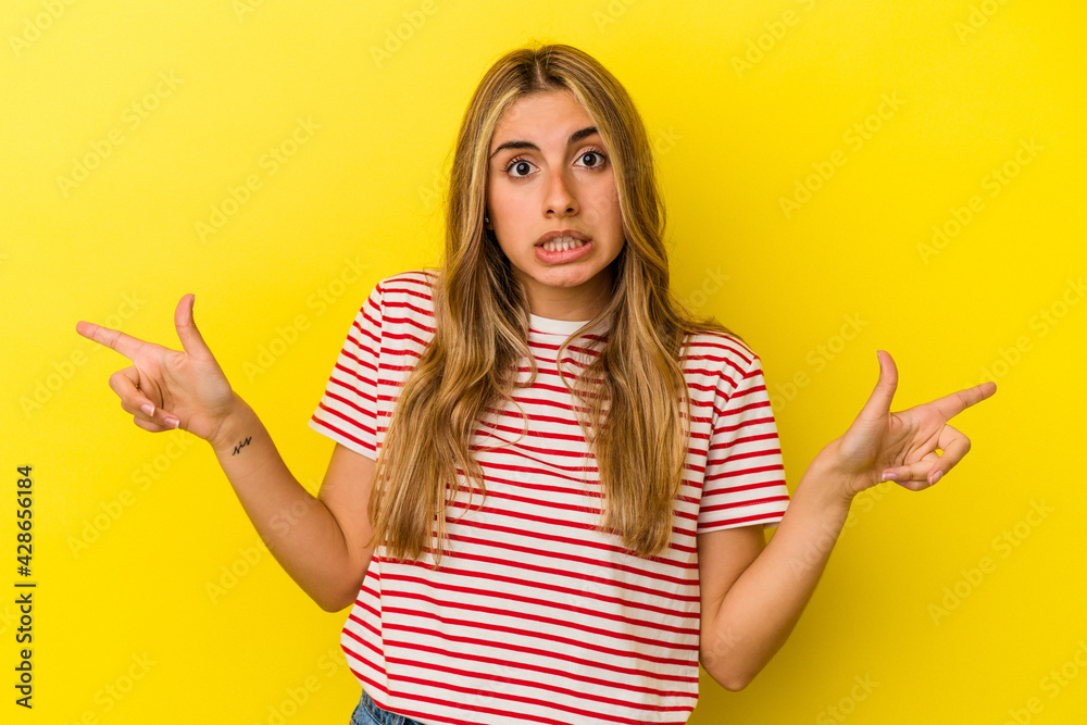 Young blonde caucasian woman isolated on yellow background pointing to different copy spaces, choosing one of them, showing with finger. Young blonde caucasian woman isolated on yellow background pointing to different copy spaces, choosing one of them, showing with finger.