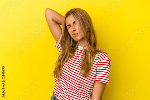 Young blonde caucasian woman isolated on yellow background having a neck pain due to stress, massaging and touching it with hand.