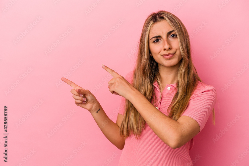 Young blonde caucasian woman isolated on pink background shocked pointing with index fingers to a copy space. Young blonde caucasian woman isolated on pink background shocked pointing with index fingers to a copy space.