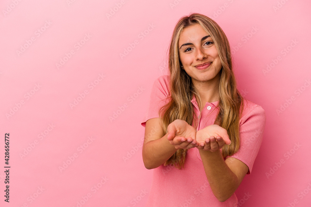 Young blonde caucasian woman isolated on pink background folding lips and holding palms to send air kiss. Young blonde caucasian woman isolated on pink background folding lips and holding palms to send air kiss.