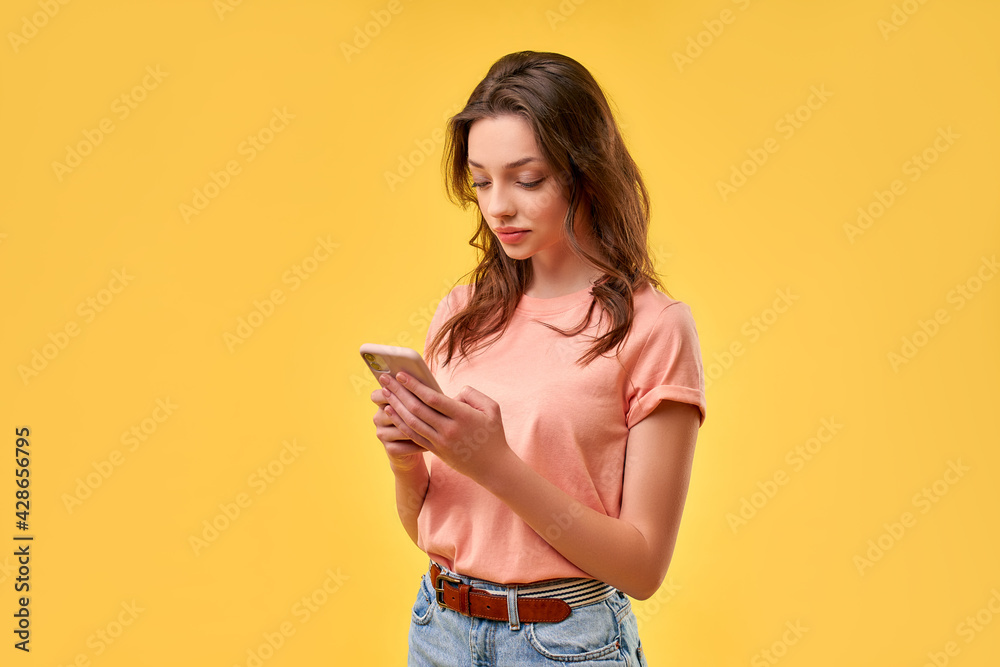 Beautiful girl in casual clothes writes a message on the phone isolated on a yellow background. Communication, always online. Beautiful girl in casual clothes writes a message on the phone isolated on a yellow background. Communication, always online.